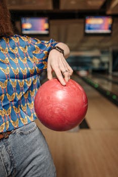 A focused woman holding a pink bowling ball at a bowling alley indoors.