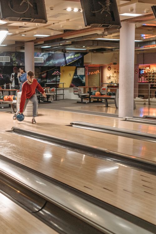 Free Adult man in red shirt holding bowling ball ready to roll down lane indoors. Stock Photo