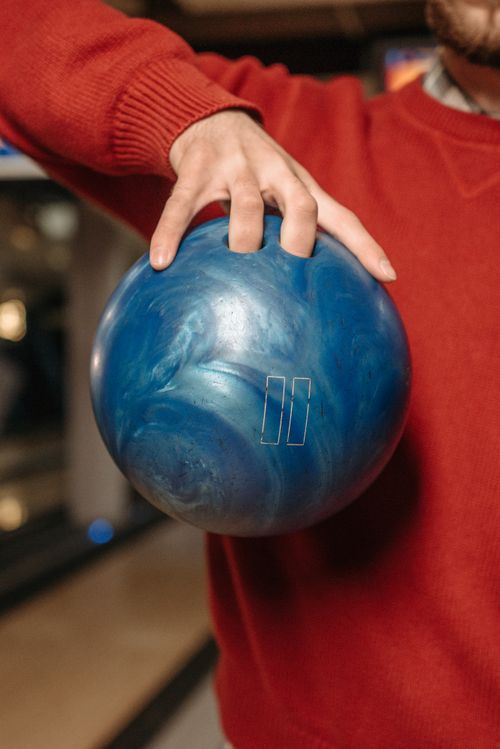 Free Person in red sweater holding a blue bowling ball in a bowling alley. Stock Photo