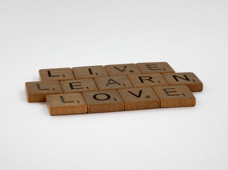 Wooden Scrabble tiles spelling 'Live Learn Love' on a white background.