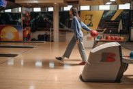 Woman bowling inside a colorful bowling alley, holding a ball in motion.