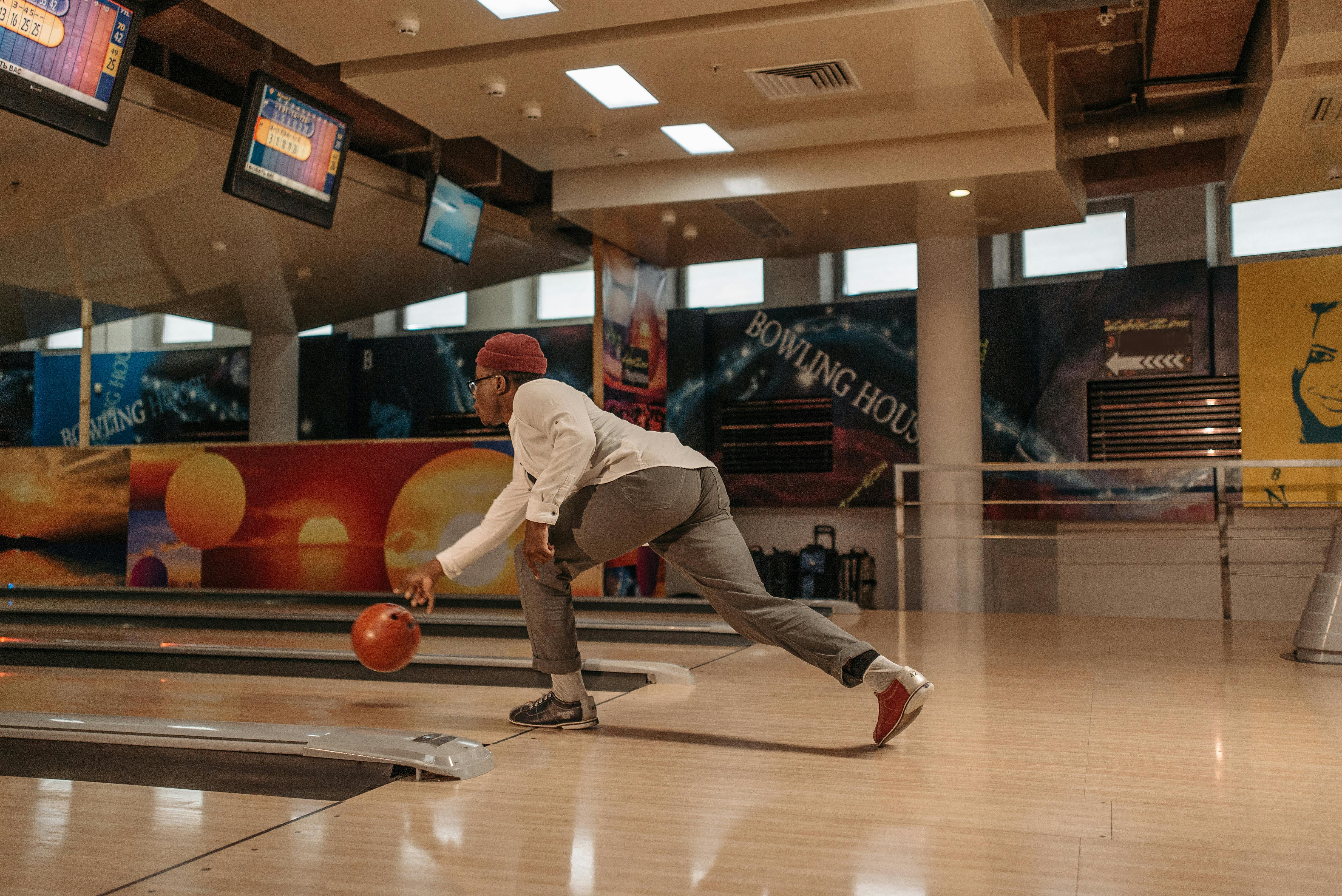 A man in a casual outfit bowls in a modern, colorful bowling alley.