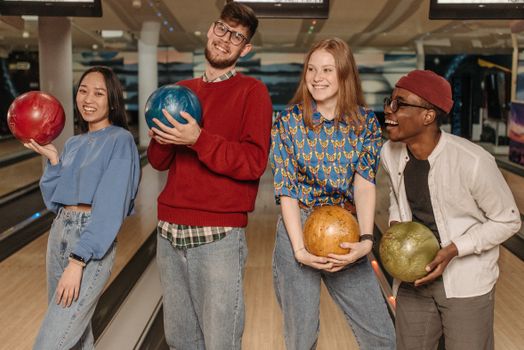 Four friends having fun at a bowling alley, holding colorful bowling balls and laughing.