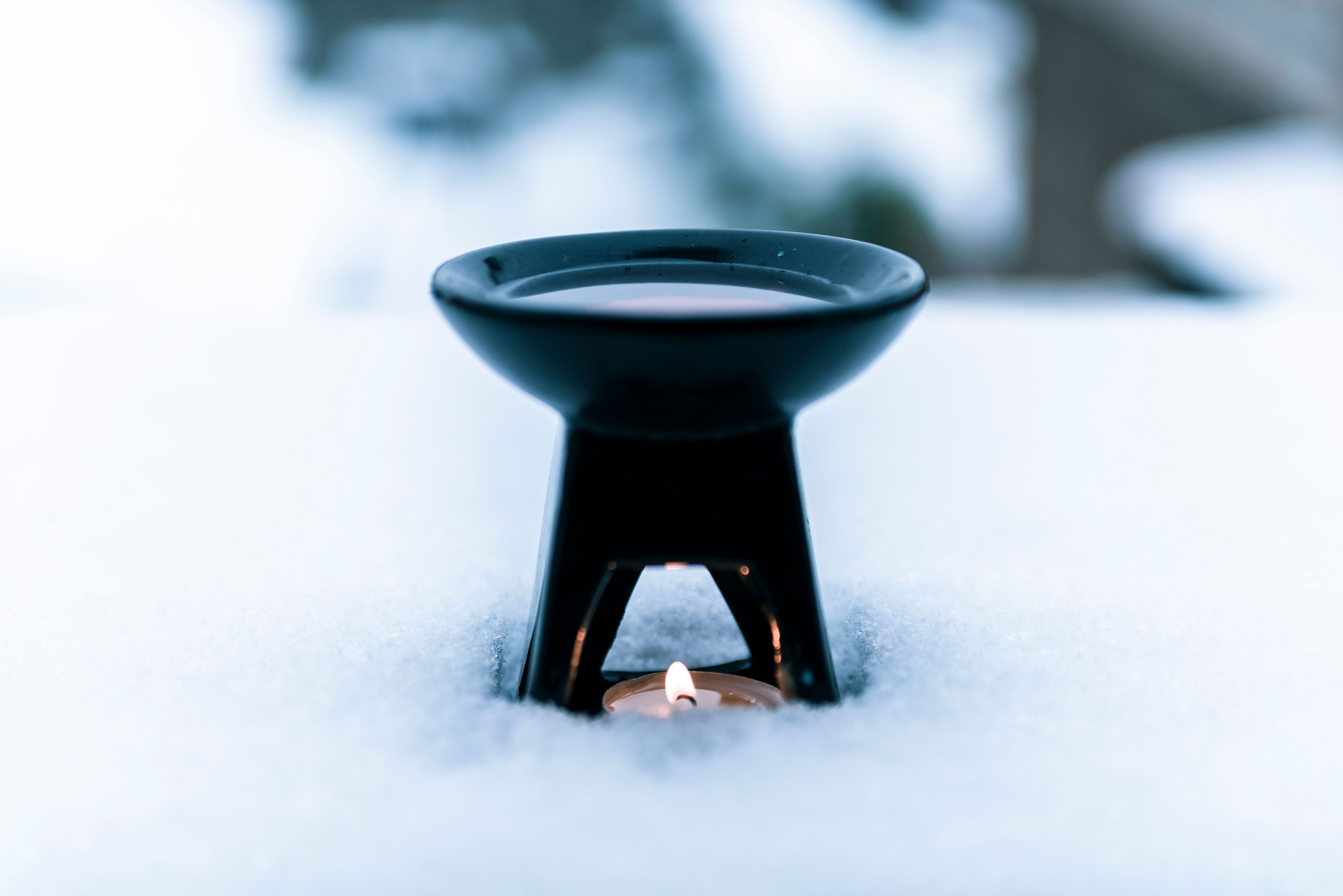 A serene winter still life featuring an aroma burner with a tealight candle surrounded by snow.