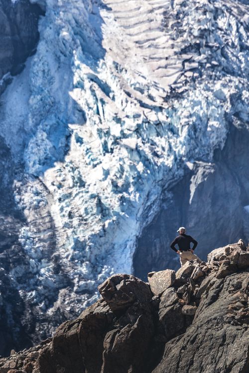 Free A lone hiker stands on rocky terrain, gazing at the majestic glacier ice in New Zealand. Stock Photo