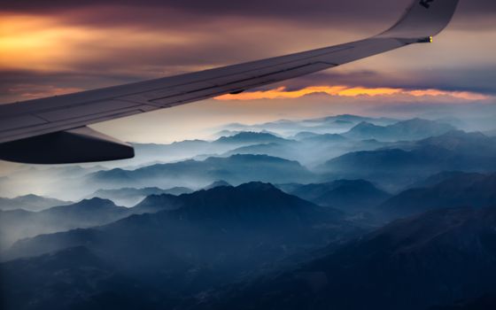 Scenic aerial view of the Swiss Alps with an airplane wing at twilight, capturing vibrant colors and misty mountains.