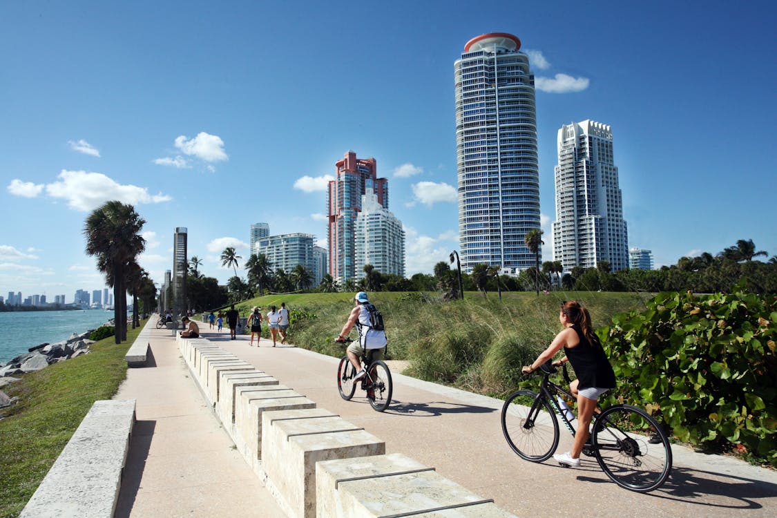 Free Cyclists ride along a scenic path in Miami Beach, with skyscrapers in the background. Stock Photo