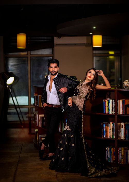 Free Stylish man and woman posing indoors against bookshelves in fashionable attire. Stock Photo