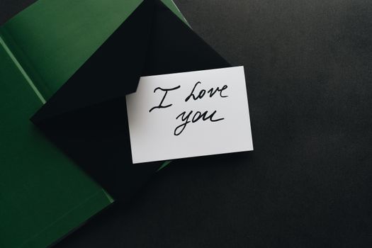 A stylish 'I Love You' note inside a dark green envelope on a flat surface.
