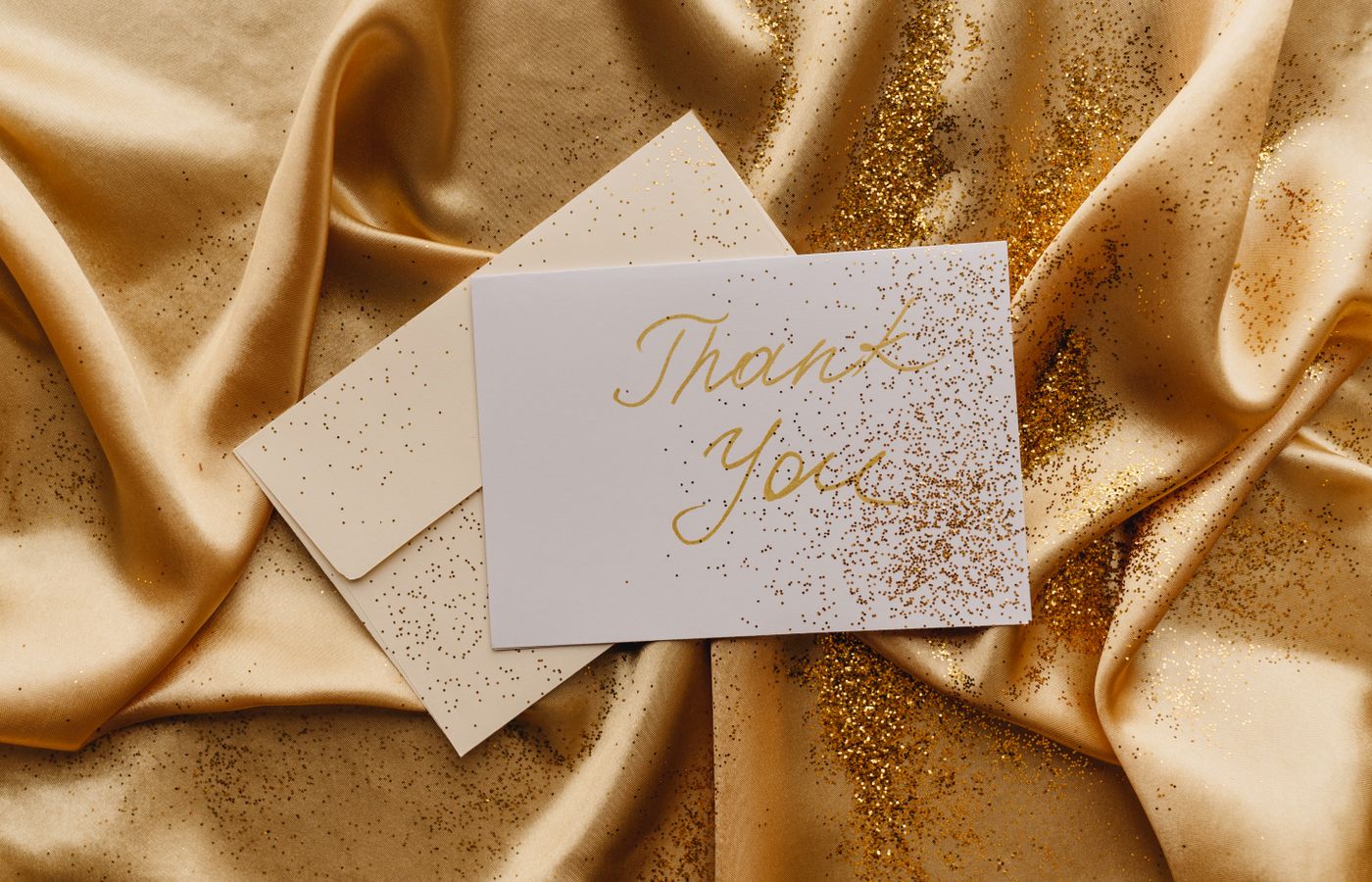Elegant thank you card displayed on gold satin with scattered glitter.