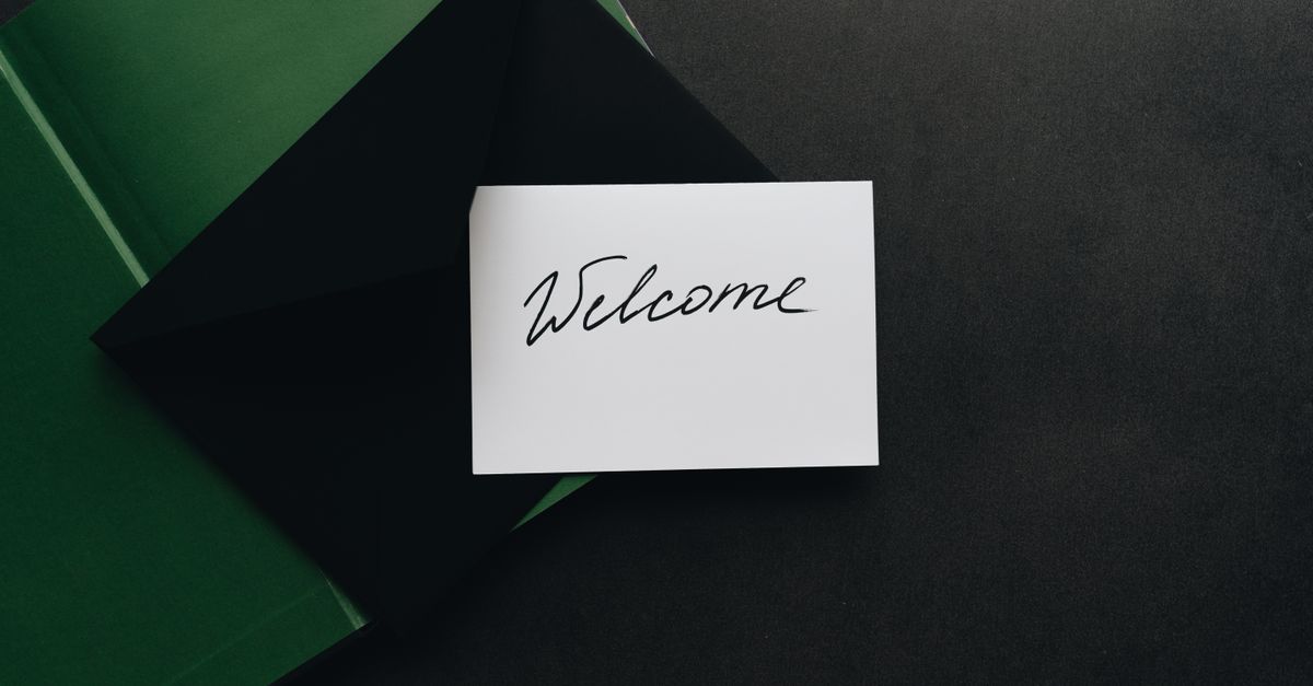 A minimalist flat lay of a black envelope with a 'Welcome' card on a dark background.