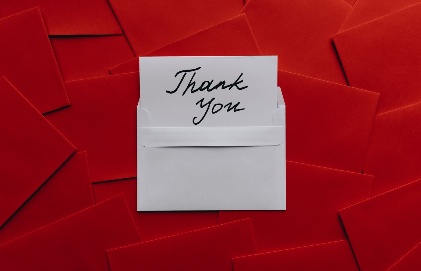Elegant thank you card in white envelope on vibrant red envelopes flatlay. Perfect for gratitude themes.