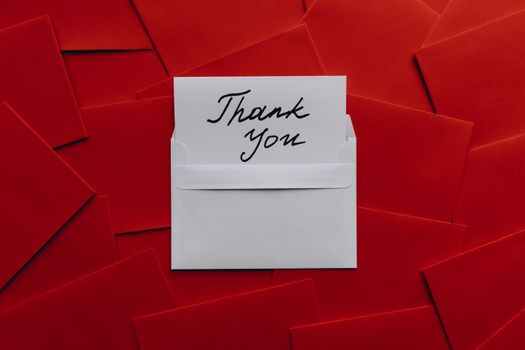 Elegant thank you card in white envelope on vibrant red envelopes flatlay. Perfect for gratitude themes.