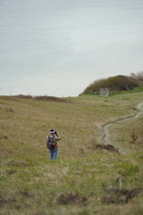 A Person in Beige Jacket Walking on Green Grass Field