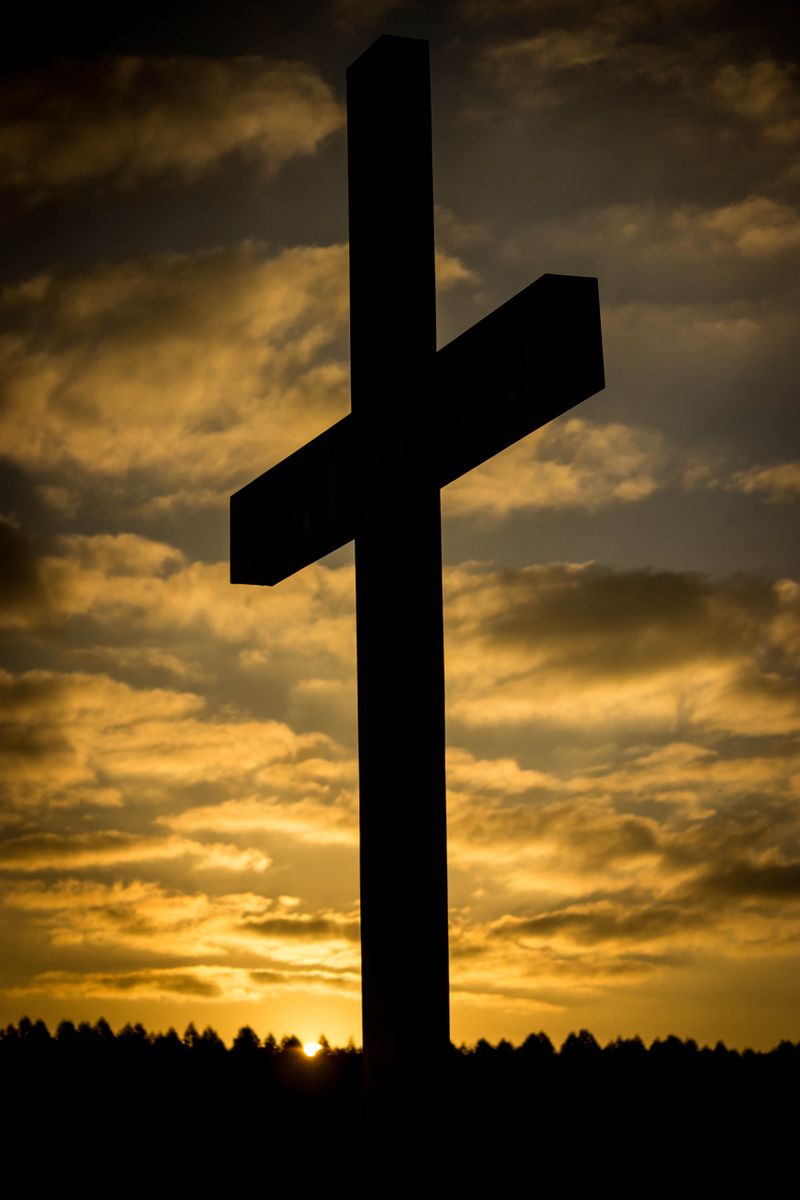 Silhouette of a cross against a dramatic sunset sky