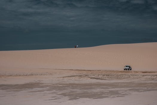 Jeep navigating the sandy dunes of Jericoacoara desert under a cloudy sky.