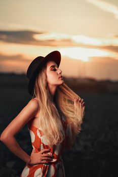A stylish woman with closed eyes poses in a hat at sunset in Birigui, Brazil.