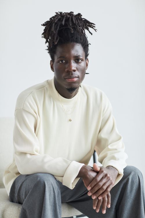 Free Stylish African American man with dreadlocks sitting indoors, exuding confidence. Stock Photo