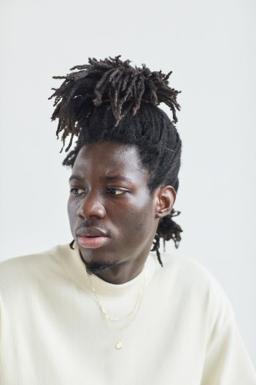 Free A serene portrait of an adult man with dreadlocks wearing a light sweater, looking away. Stock Photo