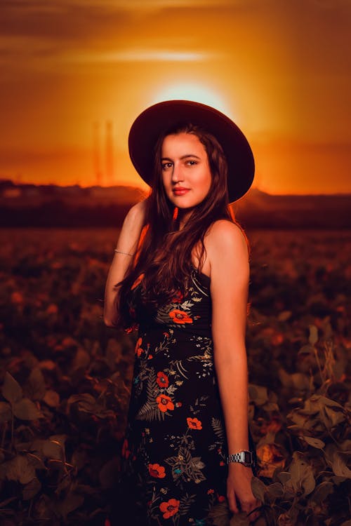 A Woman in Floral Dress Standing on the Field while Wearing a Hat