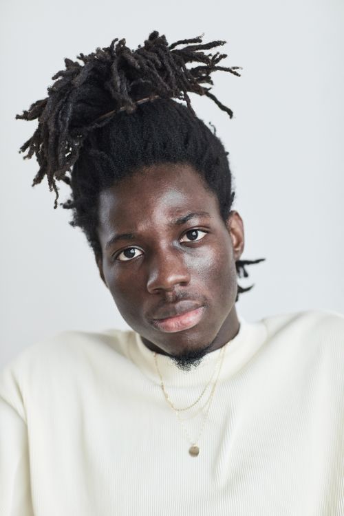 Free Close-up portrait of a man with dreadlocks wearing a white shirt in a studio setting. Stock Photo