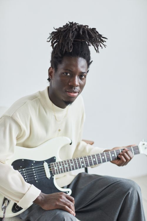 Free An adult black male playing an electric guitar indoors, showcasing his hairstyle. Stock Photo