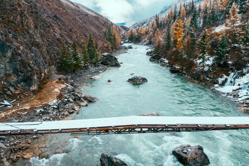 Free Snow-covered bridge over a rushing river in Altai's mountain landscape. Stock Photo