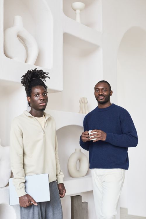 Free Two men relaxing in a modern home, one holding a laptop and the other a cup of coffee. Stock Photo