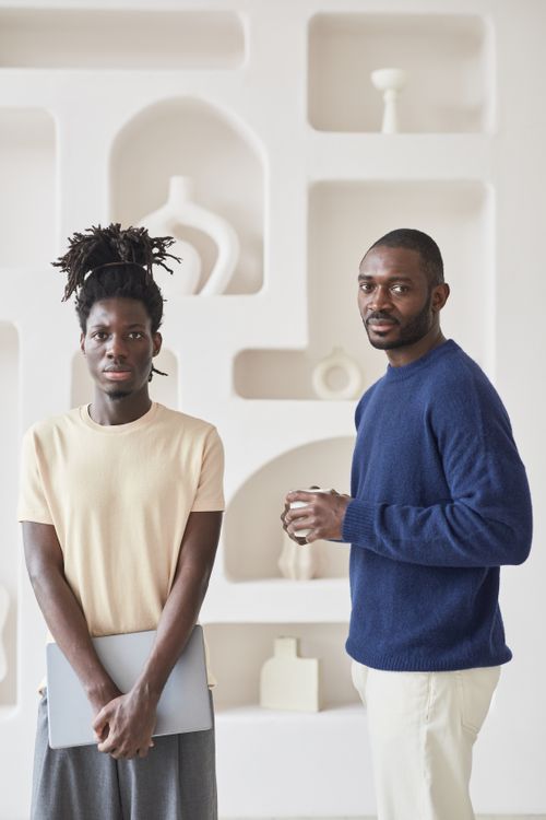 Free Two men standing with a laptop and coffee, modern interior setting. Stock Photo