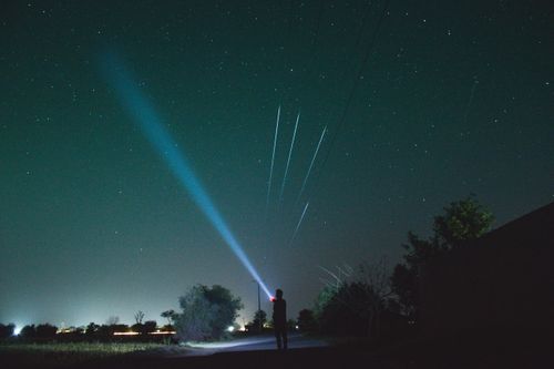 Free A person shines a flashlight towards a star-filled sky, creating a captivating silhouette against the night. Stock Photo