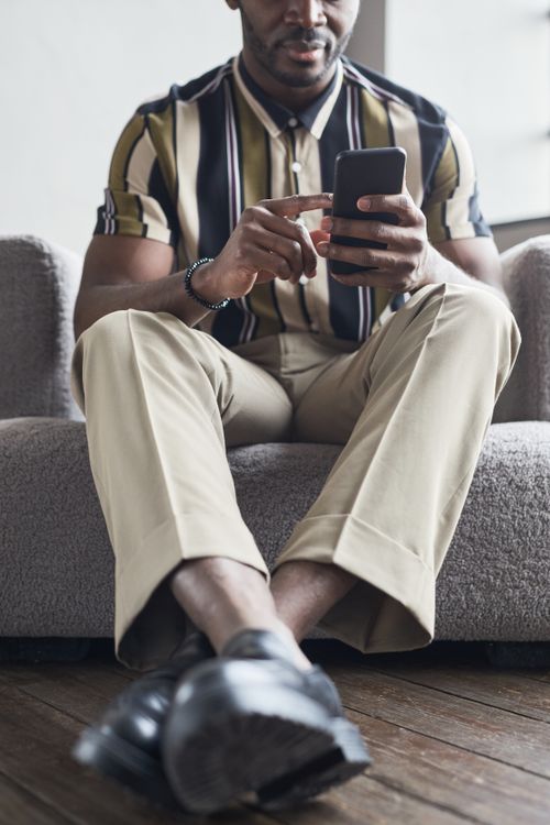 Free Fashionable man sitting on sofa using a smartphone, showcasing modern lifestyle and technology. Stock Photo