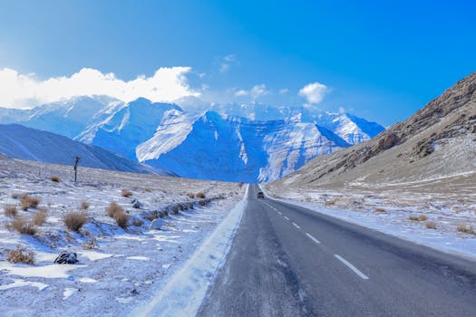 A deserted highway leads through snowy mountains under a clear blue sky, showcasing winter's beauty.