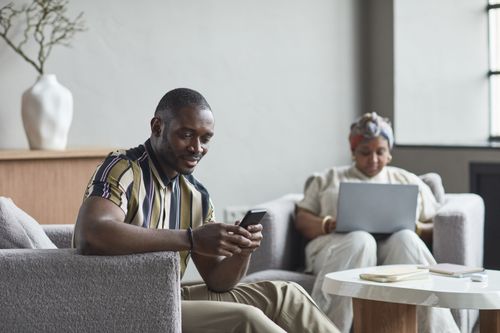 Free Two colleagues engaging with technology in a contemporary hotel lobby work setting. Stock Photo
