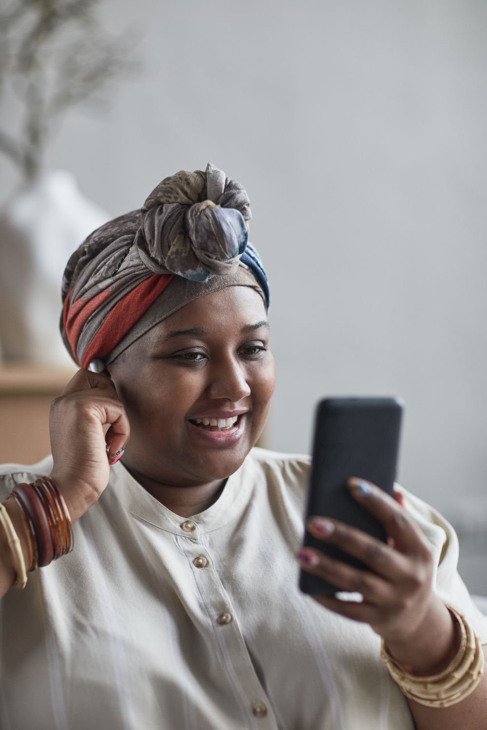 Woman in a headwrap smiling at her phone during a video call