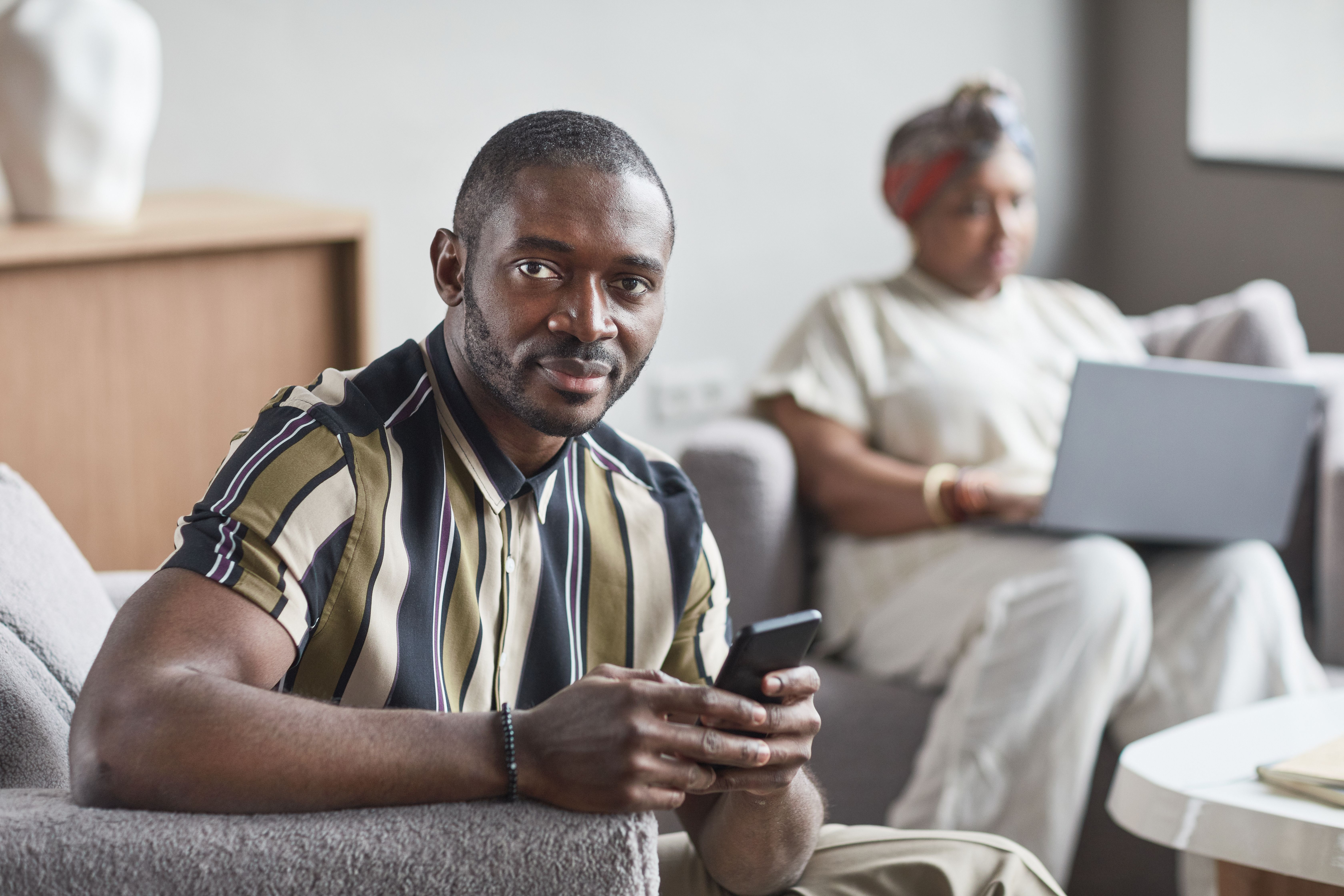 A confident man sitting indoors, calmly holding his smartphone without urgency.