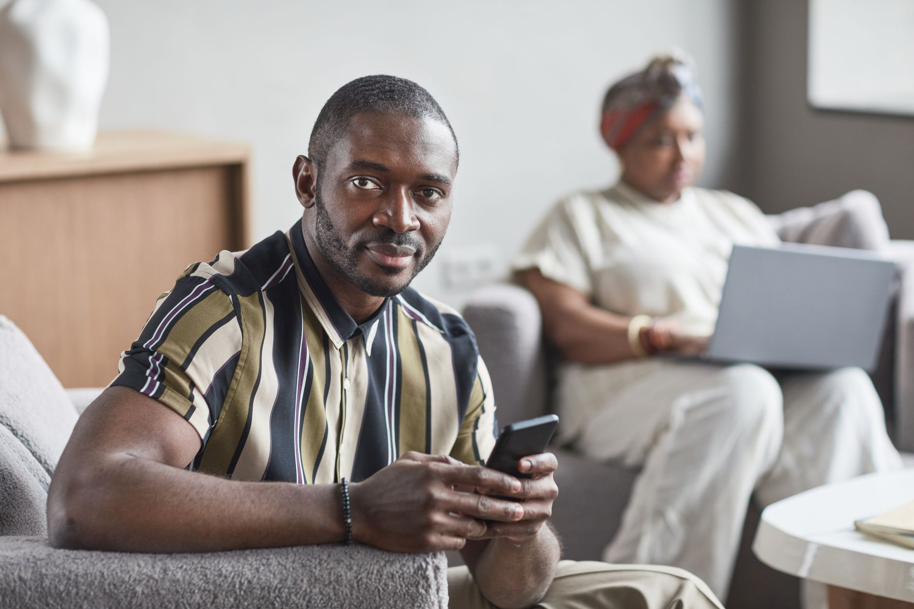 A confident man sitting indoors, calmly holding his smartphone without urgency.
