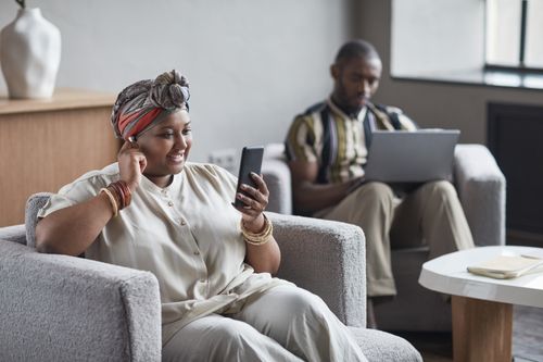 Free A woman smiling during a video chat, with a man working on a laptop in an indoor setting. Stock Photo