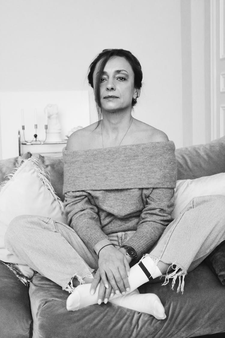 A Woman Wearing An Off Shoulder Sweater Sitting On A Couch