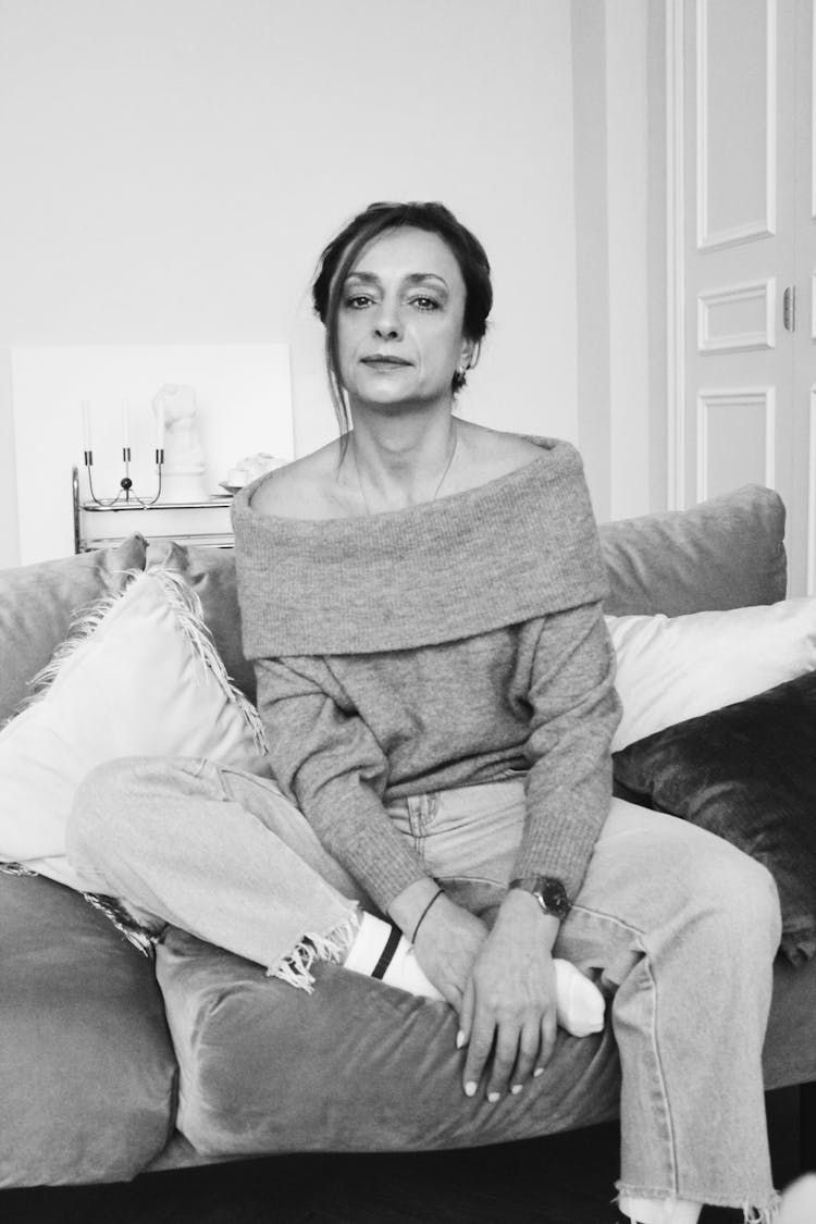 A Woman Wearing An Off Shoulder Sweater Sitting On A Couch