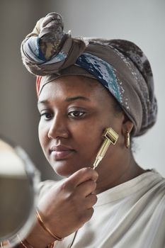 Woman using a facial roller for skincare with a headscarf, demonstrating beauty routine.