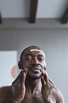 Portrait of a man applying face cream indoors as part of his skincare routine.