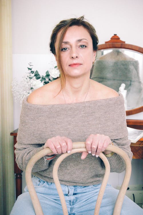Woman in Gray Off Shoulder Shirt Sitting on White Armchair
