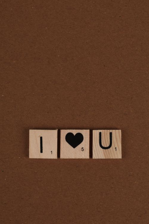 Free Three wooden Scrabble tiles on a brown background forming the message 'I love U'. Stock Photo