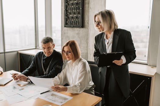A group of business professionals discussing documents at a conference table in a modern office environment.