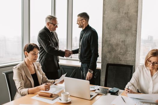 Professional business meeting with handshake in modern office room with multiple colleagues.