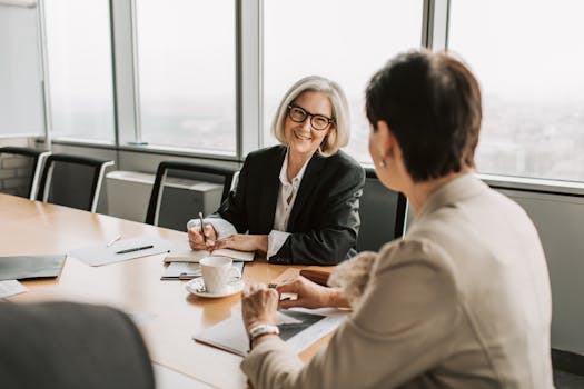 Two businesswomen in discussion during a meeting in a modern office setting.
