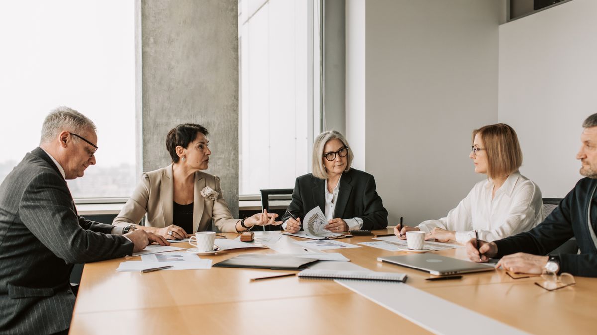 Five business professionals engaged in a meeting in a modern office setting, discussing documents and ideas.
