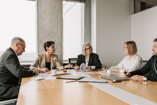 Five business professionals engaged in a meeting in a modern office setting, discussing documents and ideas.