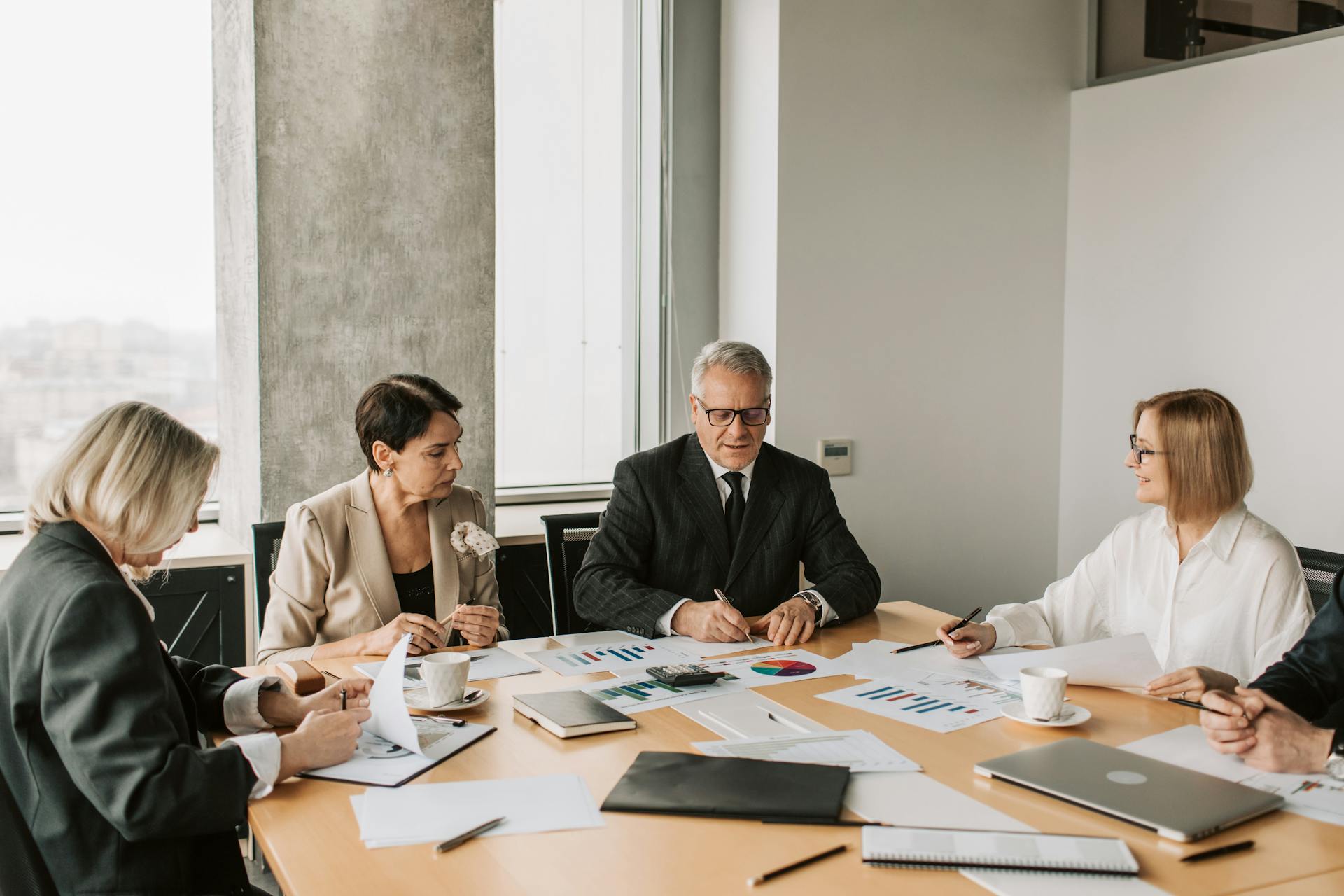 A group of professionals discussing business documents during a meeting in a modern office setting.