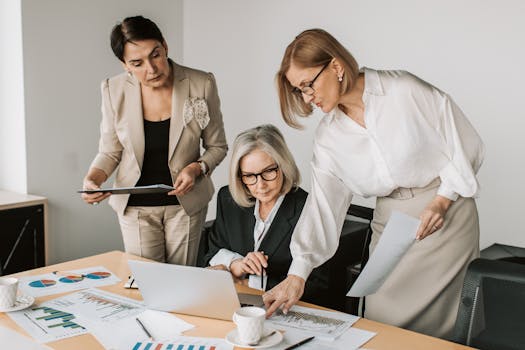 Three senior businesswomen in an office working together on a laptop and documents.